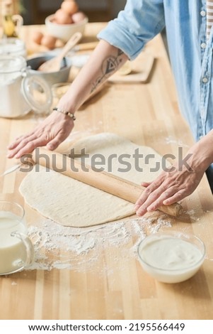Close-up of housewife working with rolling pin to roll the dough for pie at wooden table in kitchen