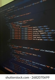 Close-up of HTML code editor on a computer screen, showing website layout and plan comparison table structure with semantic tags. Concept of web development, coding, programming, and front-end design.