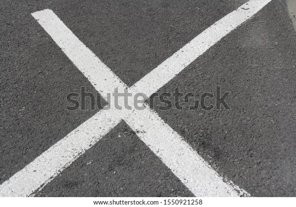 closeup of huge white painted cross\
diagonals marking prohibited area on road surface\
zone