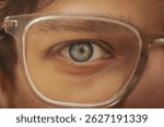 Close-up of a human eye framed by clear glasses, showcasing intricate iris detail and subtle reflection, with soft skin texture and natural lighting.