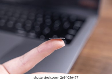 Close-up of a human finger balancing a tiny microchip component above a laptop, emphasizing advanced data storage, powerful miniaturization, and electronic computing progress