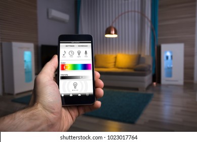 Close-up Of A Human Hand Adjusting Electric Light Through Mobile Phone At Home
