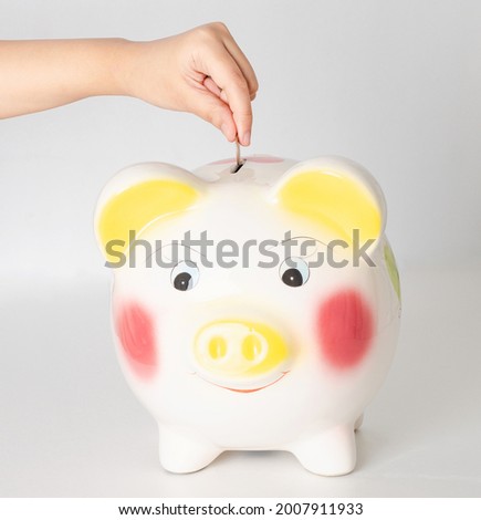 Closeup to human hand droping one coin into the piggy bank