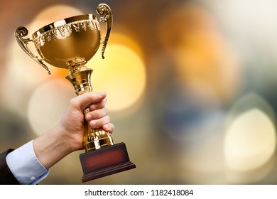 Close-up human hand holding golden Trophy on - Shutterstock ID 1182418084