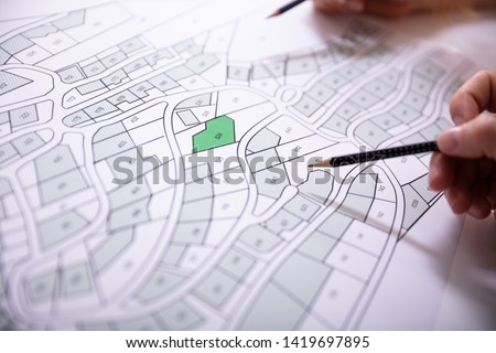 Close-up Of Human Hand Holding Pencil Over Paper Cadastre Map