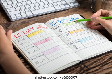 Close-up Of A Human Hand Making Exercise Plan On Notebook Over Wooden Desk