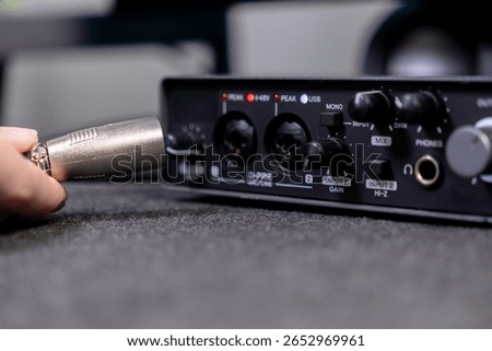Close-up of human hand plugging a silver XLR audio connector into the input jack of a digital sound card, indicating setup for studio work