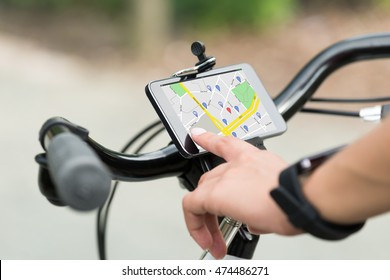 Close-up Of Human Hand Pointing At Smart Phone Showing GPS Navigation On Bicycle
