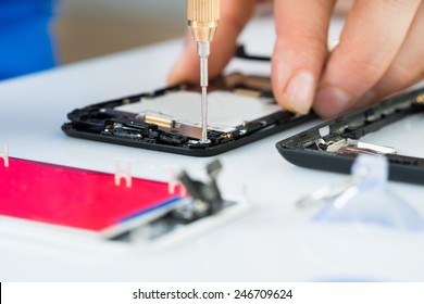 Close-up Of Human Hand Repairing Cellphone With Screwdriver On Desk