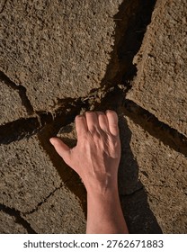 Close-up of a human hand touching deep cracks in dry soil. Concept image of drought, climate change and extreme dryness of agricultural land.