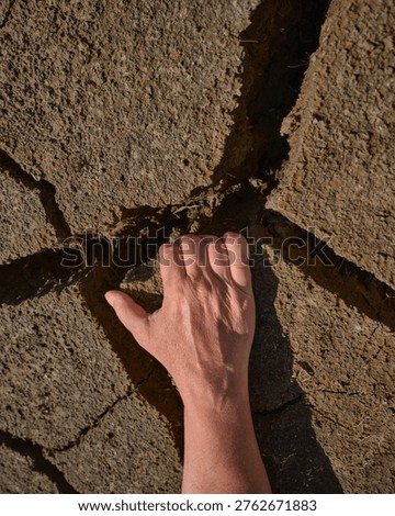 Close-up of a human hand touching deep cracks in dry soil. Concept image of drought, climate change and extreme dryness of agricultural land.