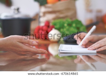 Close-up of human hands are gesticulate over a table in the kitchen. Women choosing menu or making online shopping. So much ideas for tasty cooking. Vegetarian, healthy meal and friendship concept