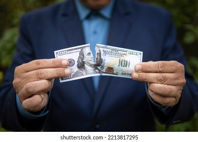 Close-up Of Human Hands Tearing Hundred-dollar Banknote. The Concept Of Losing Money And Income. A Businessman In A Jacket Tears Up A Paper Bill Of 100 US Dollars