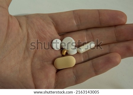 close-up: human left hand opened palm with three white round tablets one white capsule one pale yellow round tablet an one oblong pale yellow tablet captured from the top