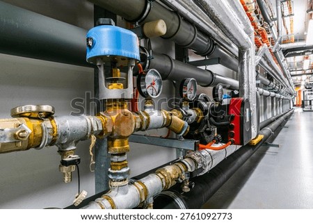 Close-up of an HVAC control assembly featuring pressure gauges, a valve actuator, and insulated piping. The setup demonstrates precise regulation of flow, pressure, and temperature in modern heating and cooling systems within industrial or commercial environments.