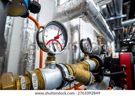 Close-up of an HVAC control assembly featuring pressure gauges, a valve actuator, and insulated piping. The setup demonstrates precise regulation of flow, pressure, and temperature in modern heating and cooling systems within industrial or commercial environments.
