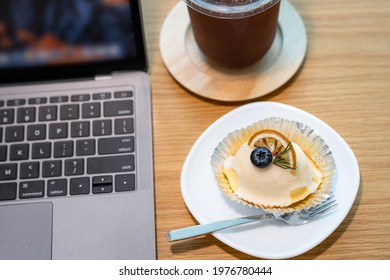 Close-up Of Ice Coffee In Cup Mug And Homemade White Orange Cake ​with Keyboard  Laptop Computer On Wood Desk Office Desk In Coffee Shop At The Cafe,during Business Work Concep