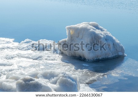 Close-up of the icy seashore, frozen waves, rocks and sun glare on the ice.