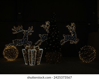 Closeup Illuminated Christmas figure, Santa Claus's reindeer and Large box gifts from bright LED garland on dark black background