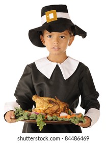 Close-up image of an adorable preschool boy in Pilgrim clothes holding a wooden platter with roast foul surrounded by colorful vegetables.  On a white background.