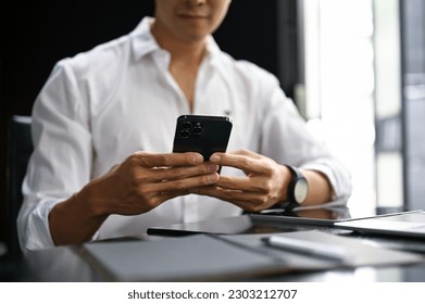 Close-up image of an Asian businessman chatting or sending sms to someone on his phone while sitting in his office. - Powered by Shutterstock