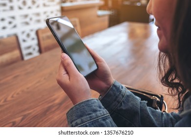 Closeup image of an asian woman holding , using and looking at smart phone in cafe
