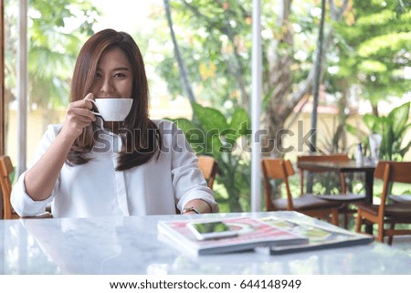 Closeup image of Asian woman smelling and drinking hot coffee with feeling good in white modern cafe