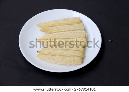 Close-up image of baby corn in white bowl on black background. A vegetable harvested early from immature corn stalks. 