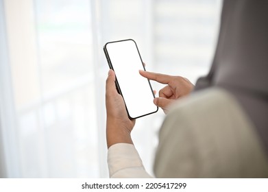 Close-up image, Beautiful Asian Muslim woman wearing hijab using her mobile phone. Phone white screen mockup in a Muslim woman's hand. - Powered by Shutterstock