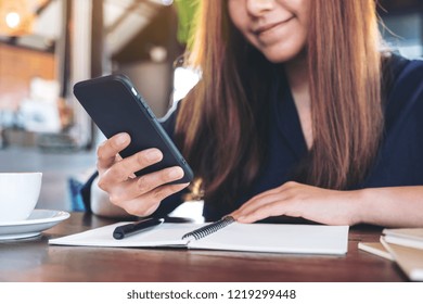 Closeup image of a beautiful asian woman holding , using and looking at smart phone while working in cafe