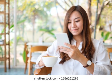 Closeup Image Of A Beautiful Asian Woman Holding And Using Mobile Phone While Drinking Coffee In Cafe