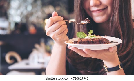 Closeup Image Of A Beautiful Asian Woman Holding And Cutting Brownie Cake With Spoon To Eat In Modern Cafe