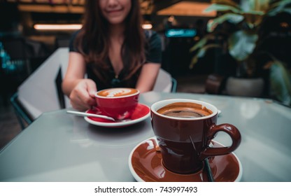 Closeup image of a beautiful Asian woman holding latte coffee cup with Americano coffee cup on glass table in loft cafe - Shutterstock ID 743997493