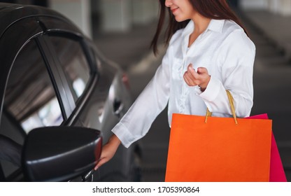 Closeup Image Of A Beautiful Woman Holding Shopping Bags While Opening Car Door In The Mall Parking Lot