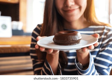 Closeup image of a beautiful young asian woman holding a plate of chocolate donut