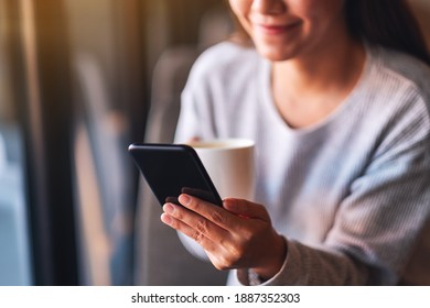 Closeup image of a beautiful young asian woman holding and using mobile phone while drinking coffee