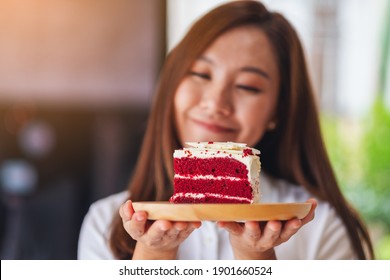 Closeup image of a beautiful young asian woman holding and eating a piece of red velvet cake in wooden tray