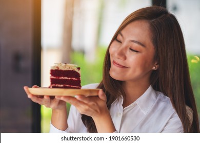 Closeup image of a beautiful young asian woman holding and eating a piece of red velvet cake in wooden tray