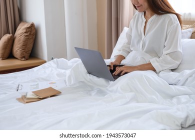 Closeup Image Of A Beautiful Young Asian Woman Using And Working On Laptop Computer While Sitting On Bed At Home