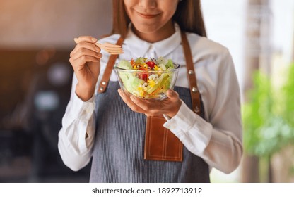 Closeup image of a beautiful young female chef holding and eating fresh mixed vegetables salad 
