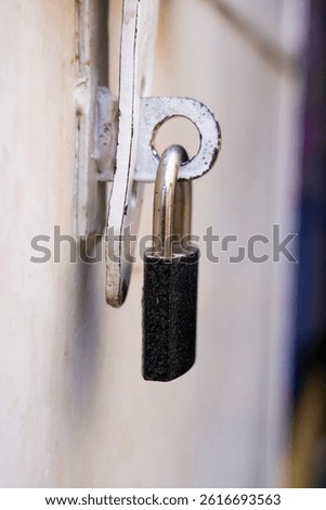 Close-up image of a black and silver lock hanging from a weathered, vintage Metal door. The aged textures and metallic contrast evoke a sense of time, tradition, and security.