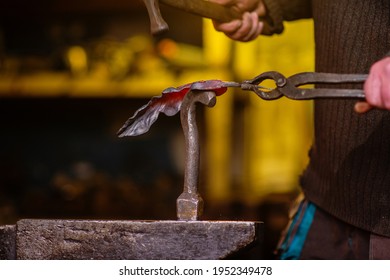 A close-up image of a blacksmith's hands forging a jewelry flower from a hot sheet of metal. Manual rework in the forge concept