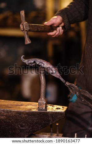 A close-up image of a blacksmith's hands forging a jewelry flower from a hot sheet of metal. Manual rework in the forge concept
