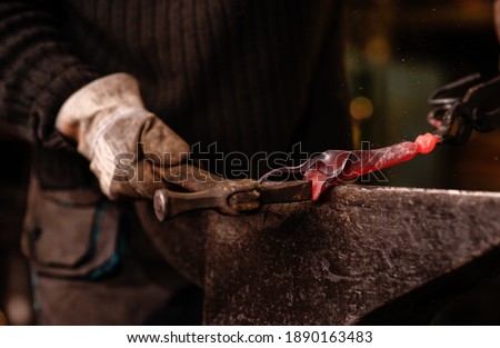 A close-up image of a blacksmith's hands forging a jewelry flower from a hot sheet of metal. Manual rework in the forge concept