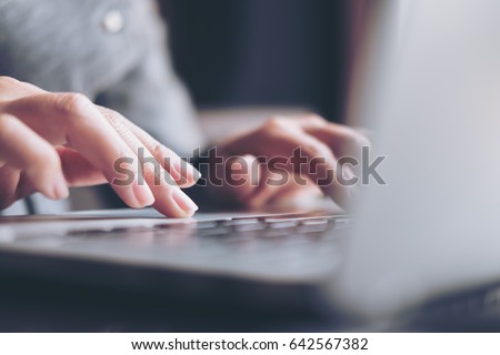 Closeup image of a business woman's hands working and typing on laptop keyboard on glass table