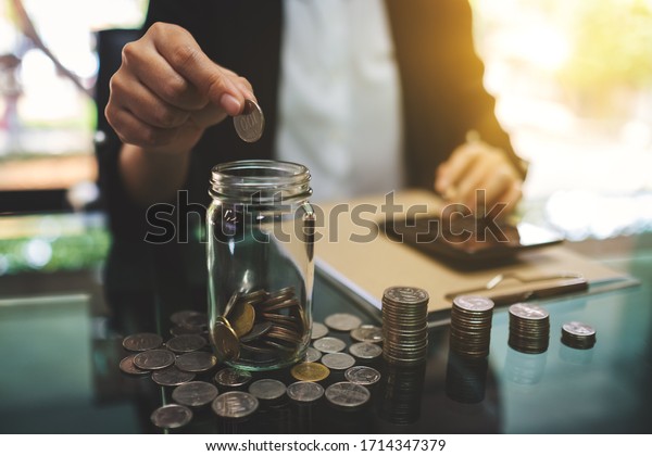 Closeup image of a businesswoman calculating, stacking and putting coins in a glass jar for saving money and financial concept