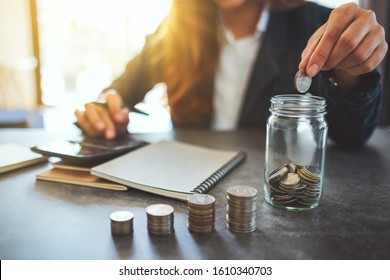 Closeup image of a businesswoman stacking and putting coins in a glass jar  - Powered by Shutterstock