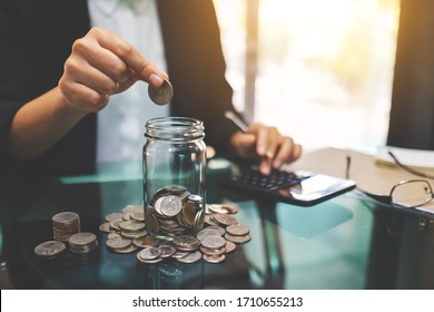 Closeup image of a businesswoman stacking and putting coins in a glass jar 
