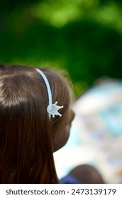  A close-up image capturing the back of a child’s head with a white crown on her head, set against a blurred natural background.