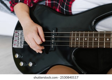 Close-up image capturing the hands of a woman in a checkered shirt playing a bass guitar, showcasing musical skill and casual style - Powered by Shutterstock